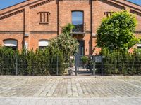 a brick building with a gate and many trees in front of it and a fire hydrant next to the gate