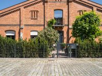 a brick building with a gate and many trees in front of it and a fire hydrant next to the gate