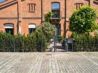 a brick building with a gate and many trees in front of it and a fire hydrant next to the gate