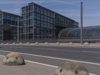 large concrete balls sitting in the curb near an empty road next to some buildings with high rises of buildings on both sides