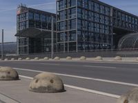 large concrete balls sitting in the curb near an empty road next to some buildings with high rises of buildings on both sides