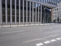 the street in front of a large building near some glass windows and people walking down it