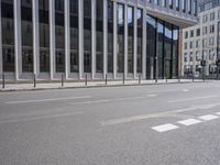 the street in front of a large building near some glass windows and people walking down it