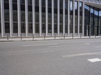 the street in front of a large building near some glass windows and people walking down it
