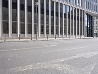 the street in front of a large building near some glass windows and people walking down it