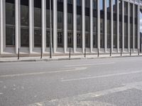 the street in front of a large building near some glass windows and people walking down it