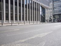 the street in front of a large building near some glass windows and people walking down it