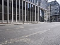 the street in front of a large building near some glass windows and people walking down it