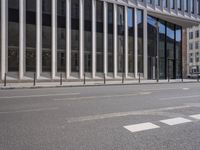 the street in front of a large building near some glass windows and people walking down it