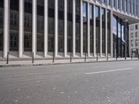 the street in front of a large building near some glass windows and people walking down it