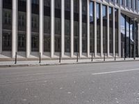 the street in front of a large building near some glass windows and people walking down it
