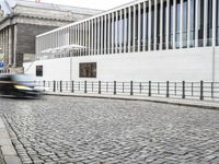 a van drives down an alley near a building and stone sidewalk with a white bus