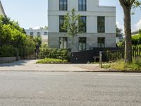 a street and a street sign in front of some trees and bushes with a building behind them