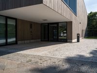 a building that has a glass door on it next to a brick sidewalk that is between trees