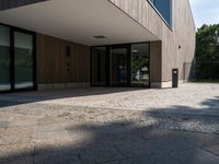 a building that has a glass door on it next to a brick sidewalk that is between trees