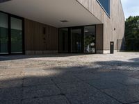 a building that has a glass door on it next to a brick sidewalk that is between trees