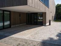 a building that has a glass door on it next to a brick sidewalk that is between trees