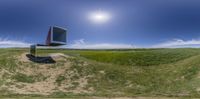 a view of a large television set in the air in a grassy field below a blue sky