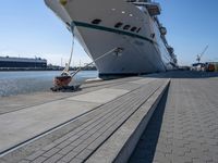 a man sits under a large cruise ship at the dock's entrance pier by himself