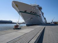 a man sits under a large cruise ship at the dock's entrance pier by himself