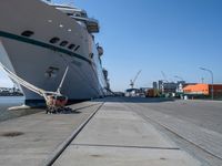 a man sits under a large cruise ship at the dock's entrance pier by himself