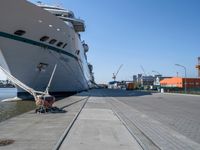 a man sits under a large cruise ship at the dock's entrance pier by himself