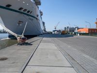 a man sits under a large cruise ship at the dock's entrance pier by himself