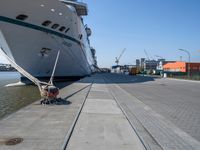 a man sits under a large cruise ship at the dock's entrance pier by himself