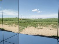 several mirrors on display on a grassy area near a field of grass with windmills