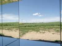 several mirrors on display on a grassy area near a field of grass with windmills