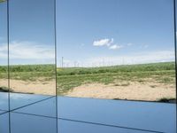 several mirrors on display on a grassy area near a field of grass with windmills