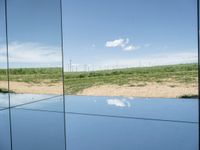 several mirrors on display on a grassy area near a field of grass with windmills