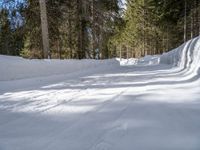 snowboarder wearing skis and riding along a snowy road lined with trees in the woods