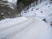 a snow - covered road in the middle of some trees and a snowy hill side
