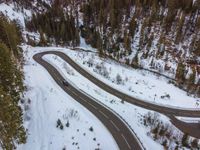 a long curved road surrounded by snow and trees in the middle of a wooded area