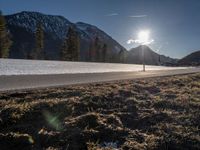 the road runs between two snowy mountains with low snow on them under the sun flare