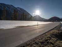 the road runs between two snowy mountains with low snow on them under the sun flare