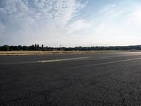 a small airplane sitting on an empty runway with trees in the background at sunset time