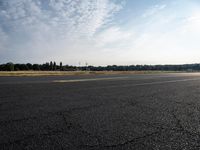 a small airplane sitting on an empty runway with trees in the background at sunset time