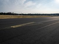 a small airplane sitting on an empty runway with trees in the background at sunset time