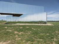 the building is mirrored in front of the grass field below the mirror fence, a woman walking