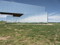 the building is mirrored in front of the grass field below the mirror fence, a woman walking