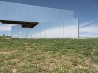 the building is mirrored in front of the grass field below the mirror fence, a woman walking