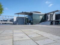 the large building has a lot of windows, and concrete bricks, around it, there is a courtyard