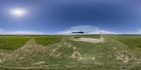 this panorama lens shows a plane flying over a grassy plain outside of a mirror with the sun behind it