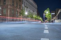 street lights are blurry in the distance in front of a tall building and tree lined street