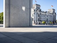 a concrete pillar in a city square and sculpture in it's center area with buildings and trees