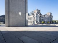 a concrete pillar in a city square and sculpture in it's center area with buildings and trees