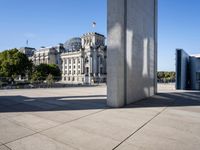 a concrete pillar in a city square and sculpture in it's center area with buildings and trees