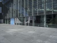 large glass and concrete building with buildings in the background reflected in windows on the outside